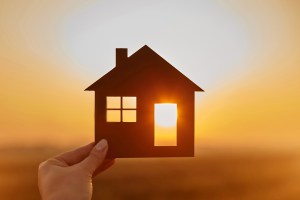 A hand holding a cutout of a home with the sun shining from behind