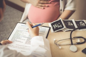 Pregnant person sits with doctor writing on a form with sonogram photos.