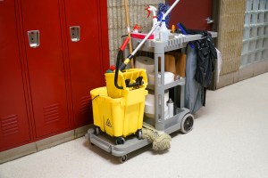 Janitorial cleaning cart with cleaning supplies in front of red lockers