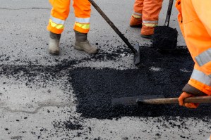 Three road crew workers flatten asphalt to repair a crack in the road.