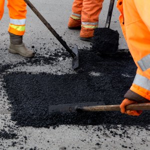 Street resurfacing by workers wearing orange uniforms using tools to spread fresh asphalt