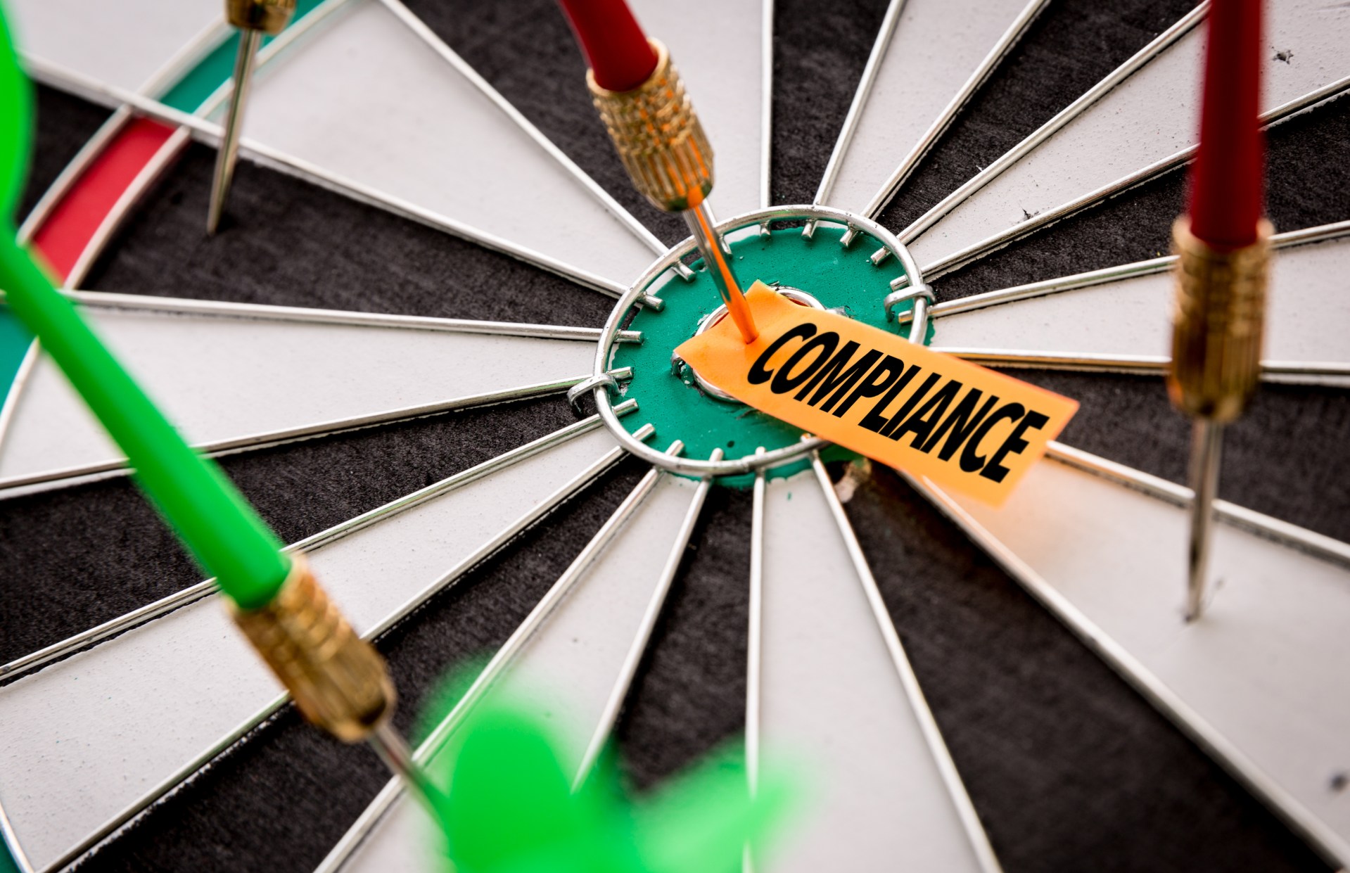 Dart on bullseye pinning paper with the word "COMPLIANCE" on the dartboard