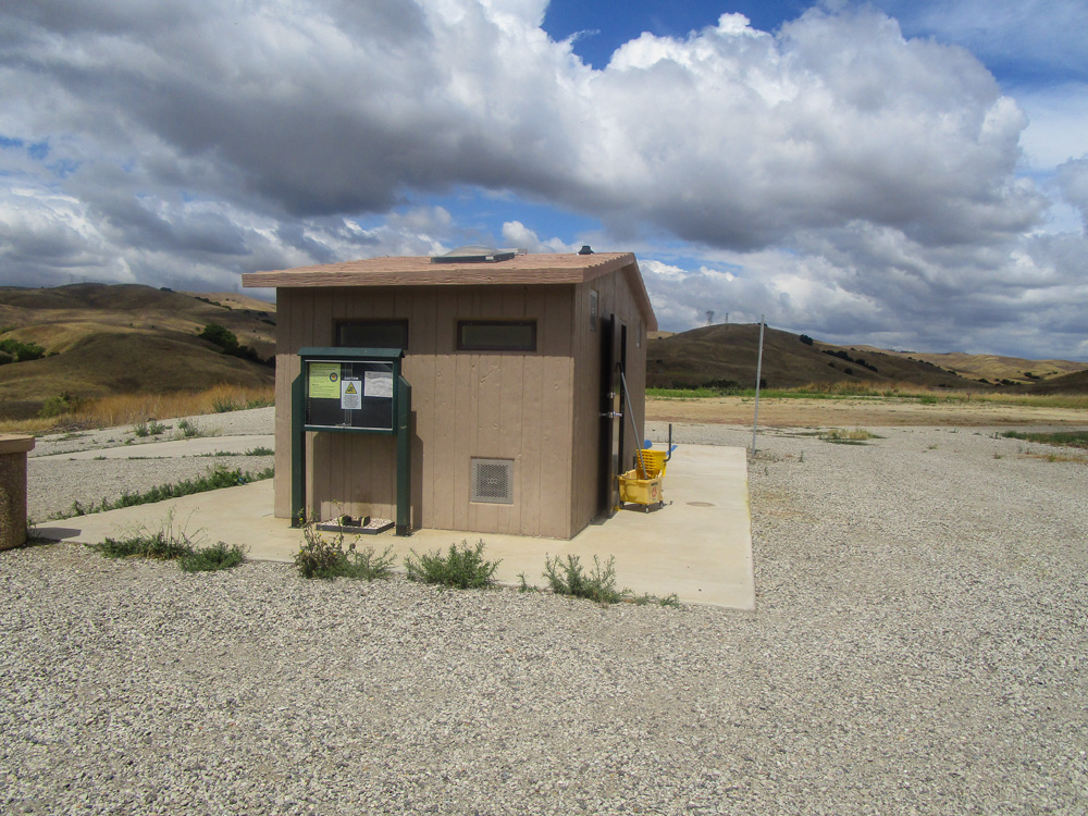 Photo 17 features a small, tan structure situated on the gravel. It is surrounded by a small square of concrete. Some green plants are growing between the concrete and the gravel.