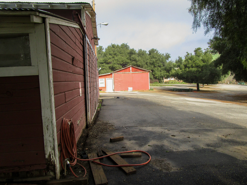 Photo 7 features a different angle of the barn; this side of the barn appears to be surrounded by concrete. There is an accompanying red structure nearby.