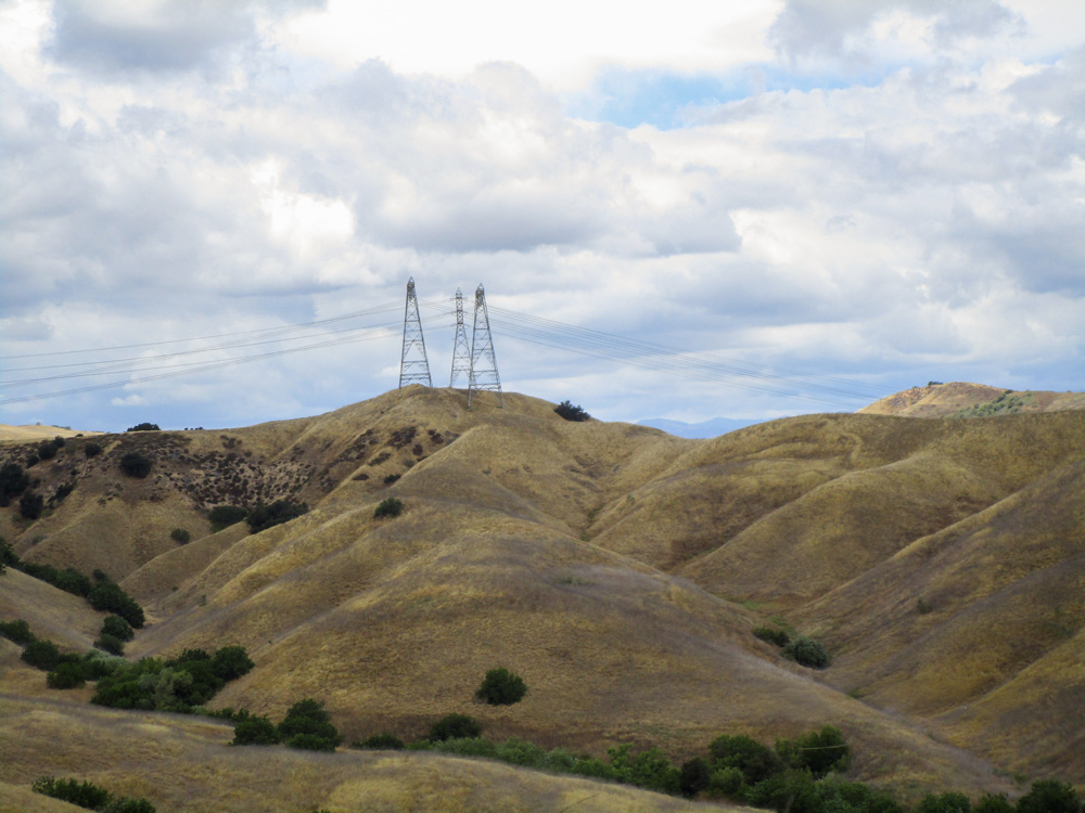 Yellow hills with tall structures atop the hills, holding transmission lines
