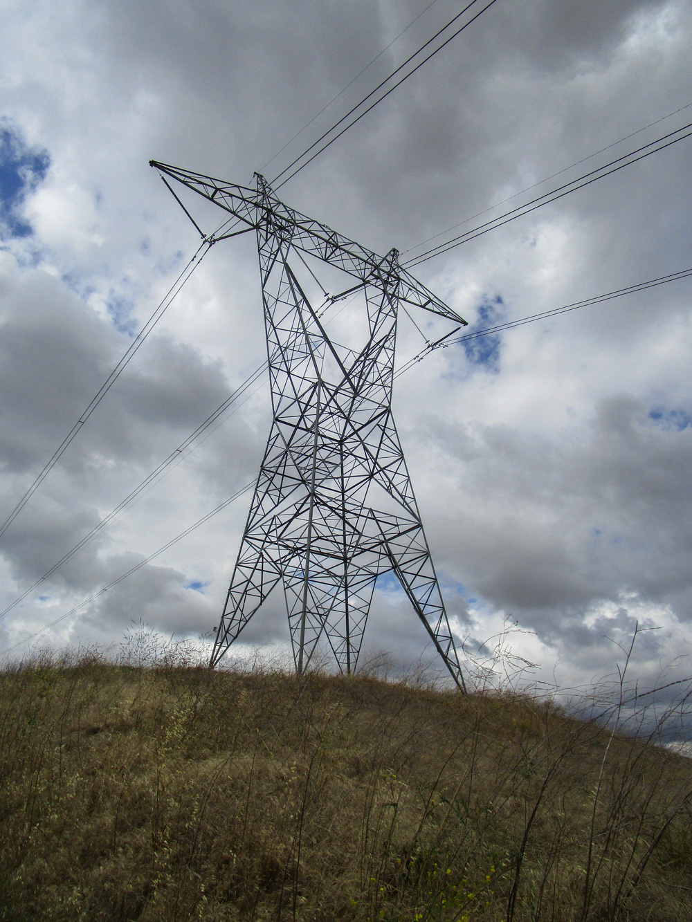 Yellow hill with tall structure atop the hill, holding transmission lines
